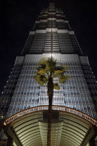 Angled view looking up at the Hyatt Hotel skyscraper illuminated at dusk with entrance arch and palm in the foreground