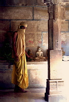 Fly monk standing near Buddha statues with a scarf covering his head and mouth