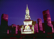 Seated stone Buddha illuminated at dusk with surrounding columns