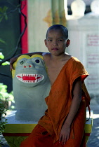 Wat Sainyamungkhun. Young monk sitting beside colourful statue at the Temple