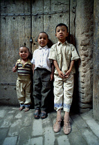 Three young boys standing against a wooden door on a cobbled street