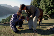 Heavenly Lake. Two men shoeing a horse near the lakeside