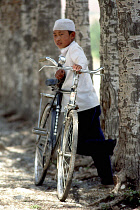 Boy standing with an adults bike in a tree lined street