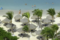 View looking down on golden sandy beach with thatched umbrellas and people walking along the waters edge