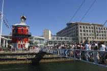 Waterfront with queue of people on a bridge crossing over to the brightly coloured clock tower