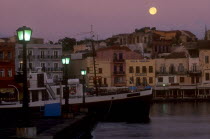 Venetian Port.  Moored boat and quayside buildings with moon in pale purple dusk sky above and illuminated street lamps.