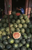 Wholesale Food Market.  Large pile of watermelon for sale  woman with arms raised in doorway behind. Asian Prathet Thai Raja Anachakra Thai Siam Southeast Asia Female Women Girl Lady Siamese Female W...