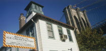 Part view of Brooklyn Bridge seen above trees with Brooklyn Ice Cream Factory building and sign in the foreground.