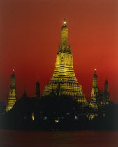 Wat Arun Temple Of The Dawn illuminated at sunset with orange sky and river in foreground