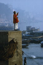 Holy man praying on stone wall above River Ganges boats town mist