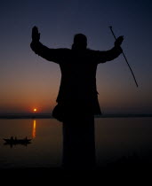 Silhouette at sunset of a Holy Man on the banks of the River Ganges with his arms outstretched  Asia Asian Bharat Inde Indian Intiya Religion Male Men Guy Religious Scenic Male Man Guy One individual...