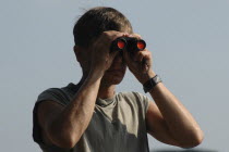 Male tourist with binoculars with scenery reflected in orange in his binoculars