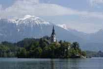 View over the lake toward Bled Island and tower of the Church of the Assumption with snow capped peaks of the Julian Alps behind