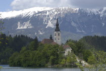 View over the lake toward Bled Island and the Church of the Assumption with the snow capped peaks of the Julian Alps behind