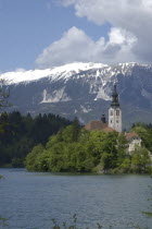 View over the lake toward Bled Island and the Church of the Assumption with the snow capped peaks of the Julian Alps behind