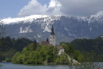 View over the lake toward Bled Island and the Church of the Assumption with the snow capped peaks of the Julian Alps behind