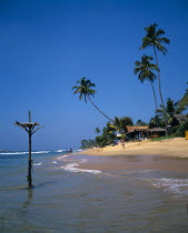 View along sandy beach with overhanging palms toward beach front restaurant and fishermans perch in the foreground