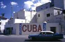 Street scene with passing classic car and the words Viva Cuba painted on the wall opposite