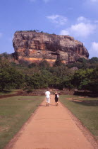 View towards huge monolithic rock site of fith century citadel.  Also called Lion Rock.  Tourist couple on path through gardens in the foreground.