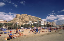 Busy beach scene with clifftop castle beyond