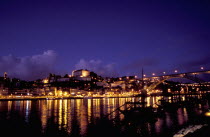 View over silhouetted boats moored in the port toward the city illuminated at dusk