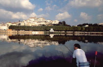 Man fishing on the bank of the River Mondego with the University crowning Alcacova Hill opposite