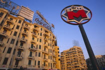 Sadat metro station sign on Midan Tahrir with city buildings and advertising for Coca Cola and Kentucky Fried Chicken behind.