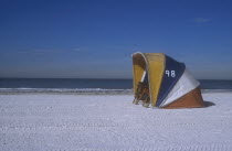 Clearwater beach with two empty deckchairs shielded by a brightly coloured windbreak.