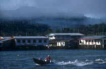 Morning mist rising from the jungle behind the kampong stilt house village with a water taxi on the river in the foreground