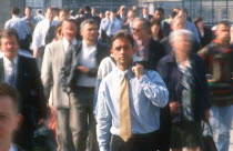 City businessman in shirt and tie holding suit jacket over his shoulder standing motionless surrounded by crowds in blurred movement.