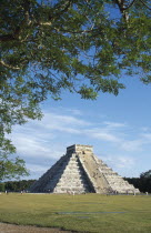 El Castillo  angled view of facade partly framed by tree branches with visitors climbing steep steps to the top.