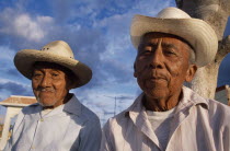 Two smiling  elderly men in hats  head and shoulder portraits one slightly behind other.