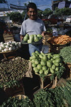 Male vendor standing behind display of vegetables at market.