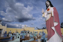 Cemetery with painted religious statue in the foreground and graves painted blue and turquoise behind.