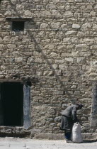 Man tying sack in the street beside a stone building