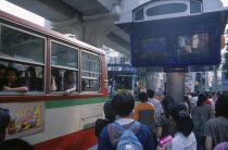 Bus and passengers at bus stop in Siam Square beside one video screen showing bus times and another a music video