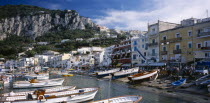 Marina Grande.  View over moored boats in harbour lined with colourful houses and busy cafes and restaurants.  Rocky hillside behind.