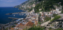 View over red tiled roof tops of the town with the Duomo bell tower at its centre towards the harbour and rocky coastline.