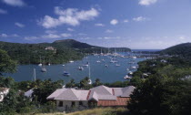 View over house rooftops towards bay with moored yachts and surrounding coastline.