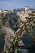 Wooden norias or waterwheels on the Orontes river and the Al-Nuri Mosque dating from 1172 and built of limestone and basalt.  Large section of a wheel in the immediate foreground.