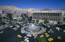 View over Tajrida Al Maghribiya Square with traffic encircling a central fountain.  Modern facade of the Central Bank top right.