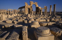 Monumental arch.  High central arch flanked by a lower arch on each side with colonnaded street part seen  behind and masonry ruins in the foreground. Palmyra Palmyra