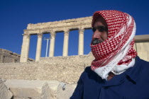 Custodian to the Sanctuary of Bel in traditional red and white checked head-scarf gutra or kiffeiya.  Ruins of colonnaded portico behind.