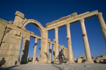 Colonnade and archway with man on a bicycle framed between columns.