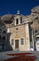 Deir Martalka  the Convent of St Takla.  Exterior and bell tower with flower petals laid out on rugs in the courtyard and steep  eroded cliff face behind.