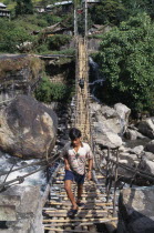 Near Besisahar.  Young man crossing wood and rope foot bridge over rocky river gorge.