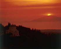 View past domed church in rural landscape to sun setting behind an island out at sea  view from Zia Taverna