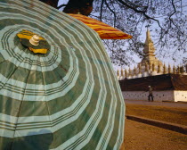 Pha That Luang Sacred Stupa with large green striped umbrella in foreground.