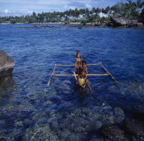 Children in outrigger canoe on clear dark blue sea  rocks palms