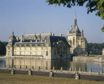 Chantilly Chateau with its reflection in surrounding water and a road in the foreground